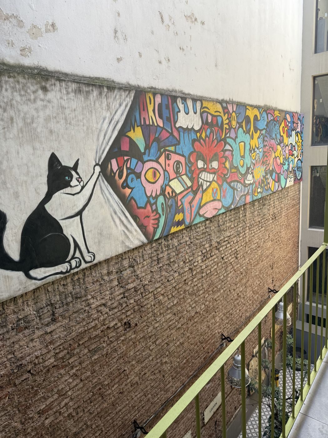 El mural del patio: un gato blanco y negro corre una cortina de colores a lo largo de la pared de ladrillo